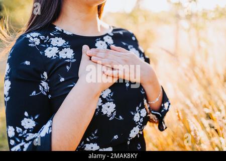 Eine hoffnungsvolle Frau, die ihr Herz in Dankbarkeit für Gottes Segen auf dem Feld anfasst. Speicherplatz kopieren Stockfoto