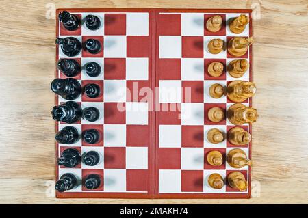 Blick von oben auf ein kleines klassisches Schachset aus Holz und Brett auf einem Holztisch. Das Bild kann zur Platzierung wie gewünscht gedreht werden. Stockfoto