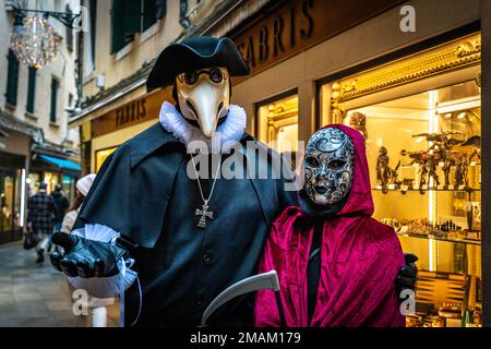 Ein Mann in einem Pestdoktorkostüm und eine Frau in einem Totenkostüm auf einer Abendstraße in Venedig, Italien Stockfoto