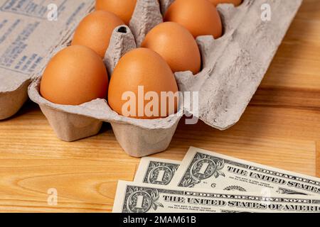 Frische braune Hühnereier in einem Karton mit Bargeld. Eierpreis, Lebensmitteleinkauf und Geflügelzuchtkonzept. Stockfoto