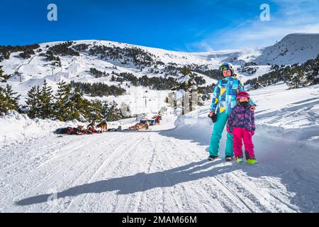 Mutter und Tochter, Skifahrer, auf einer verschneiten Straße, Huskey Hundeschlittenfahrten, Berge und Wald im Hintergrund. Winterurlaub, Andorra, Pyrenäen Stockfoto