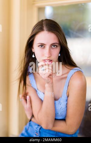Teenager-Mädchen sitzt und beißt Lippe und dreht sich zur Gesichtskamera Stockfoto