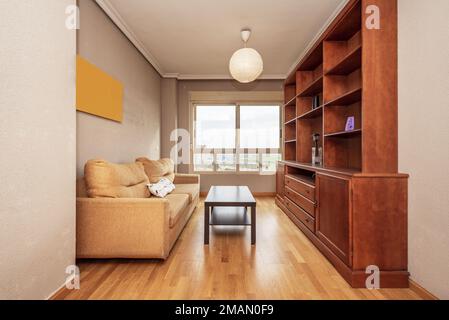 Kleines Wohnzimmer mit rötlichem Holzregal, senffarbenem Dreisitzer-Sofa und einem Fenster mit Aussicht Stockfoto