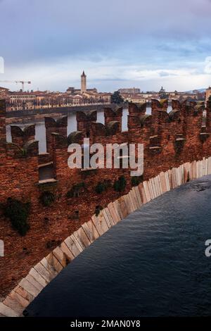 Verona, Italien, Januar 2023. Eine einsame Figur unter einem Schirm überquert die Brücke Ponte Scaligero über den Fluss Adige in einem stimmungsvollen Stadtbild. Stockfoto