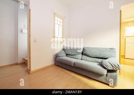 Wohnzimmer eines Hauses mit einem einsamen Zweisitzer-Sofa mit blauer Polsterung und einem weißen Holzfenster mit durchsichtigem Glas Stockfoto