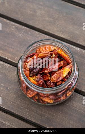 Ein durchsichtiges Glasgefäß ohne Deckel mit getrockneten Chilipaprika auf Akazienholzoberfläche Stockfoto