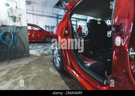 Rotes Auto mit offener Tür, das zur Wartung und Reparatur in einer Autowerkstatt geparkt ist. Hochwertige Fotos Stockfoto