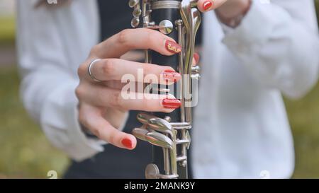 Ein Mädchen spielt im Sommer Klarinette im Park. Nahaufnahme ihrer Hände. Stockfoto