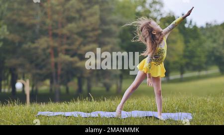 Ein kleines Mädchen führt die Elemente der rhythmischen Gymnastik im Park auf. Stockfoto