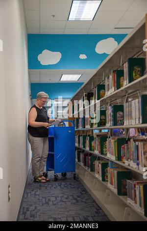 Holly Keene-Steele, eine Bibliothekstechnikerin, durchsucht ihre Liste mit Kinderbüchern, die sie in einem Wagen in der John L. Throckmorton Library in Fort Bragg, North Carolina, am 1. Juni 2022 aufbewahren kann. Bücher, die für Kinder als leichter lesbar gelten, werden häufig aus der Kinderabteilung herausgenommen und später an der Rezeption der Bibliothek für Eltern organisiert. Stockfoto