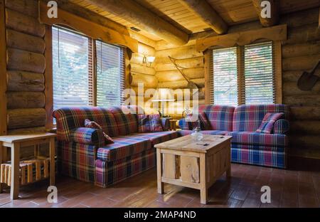 Rote und blaue Schottensofas mit rustikalem Holzkästen-Couchtisch im Wohnzimmer im Blockhaus im skandinavischen Stil. Stockfoto