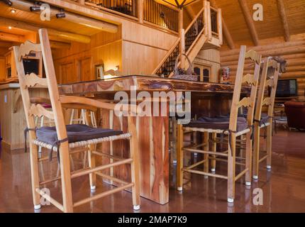 Hölzerner Esstisch und gewebte Sitzstühle mit hoher Rückenlehne mit braunen Kissen im Speisesaal im Blockhaus im skandinavischen Stil. Stockfoto