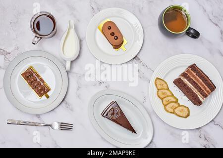 Einige Desserts und Kaffee auf einem Marmortisch mit weißen Tellern, silbernen Löffeln und zwei verschiedenen Arten von Kuchen Stockfoto