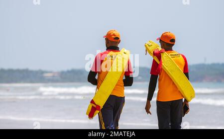 Zwei Rettungsschwimmer am tropischen Strand, die beide Rettungsrohre auf ihren Schultern tragen und in Weligama, Sri Lanka, spazieren gehen. Stockfoto