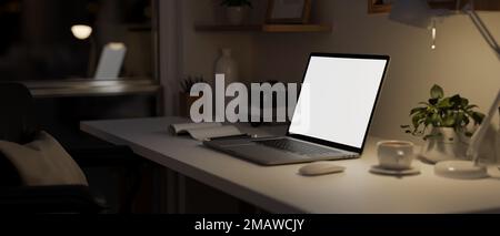 Seitenansicht, modernes Home Office bei Nacht mit tragbarem Notebook-Laptop-Modell mit weißem Bildschirm, Licht von Tischleuchte und Zubehör auf weißem Tisch. 3D ren Stockfoto