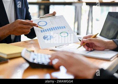 Intelligenter und professioneller asiatischer Geschäftsmann, der Finanzdaten mit seinen Kollegen erläutert und diskutiert und im Büro zusammenarbeitet. Zugeschnittenes Bild Stockfoto