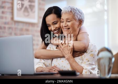 Erst sparen wir, dann Viel Spaß. Eine ältere Frau, die mit ihrer Tochter zu Hause einen Laptop benutzt. Stockfoto