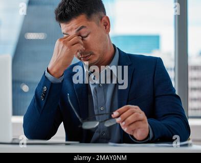 Das ist ein wahrer Albtraum. Ein gutaussehender junger Geschäftsmann, der allein im Büro sitzt und gestresst ist, während er sein Notebook benutzt. Stockfoto