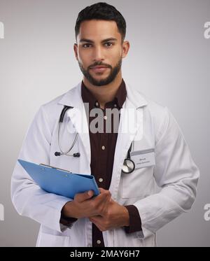 Was tun Sie, wenn ich Leben rette? Ein gutaussehender junger Arzt, der allein im Studio steht und ein Klemmbrett in der Hand hält. Stockfoto