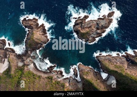 Blick von oben, atemberaubender Blick auf eine felsige Küste mit einigen Meereswellen, die am Ufer zerquetschen. Lombok Island, West Nusa Tenggara, Indonesien. Stockfoto