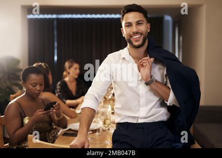 Wir begrüßen das neue Jahr mit der Klasse. Ein gutaussehender junger Mann steht und hält seine Jacke während einer Silvester-Dinner-Party mit Freunden in der Hand. Stockfoto
