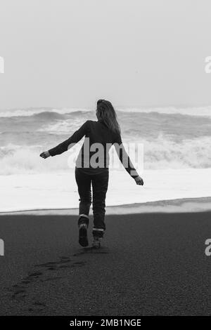 Glückliche Frau, die am schwarzen Strand entlang geht, einfarbige malerische Fotografie Stockfoto