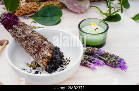 Verwischen Sie den Stab mit Kerze und Lavendel auf einem Tisch mit Pflanzen und Kristallen Stockfoto