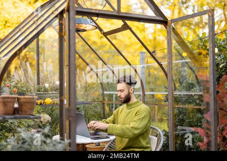 Mann arbeitet fernab auf Laptop im Glashaus im Hinterhof Stockfoto