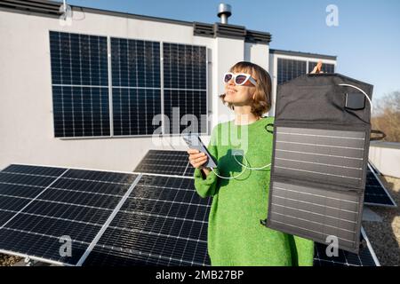 Frau lädt Handy von einem tragbaren Solarmodul Stockfoto