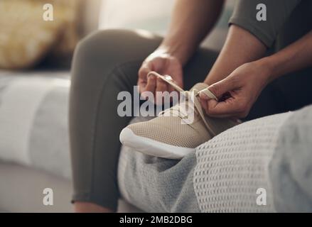 Es ist Zeit, auf die Rollbahn zu fahren. Eine unbekannte Frau, die zu Hause allein auf ihrem Sofa sitzt und sich vor dem Training die Schnürsenkel bindet. Stockfoto