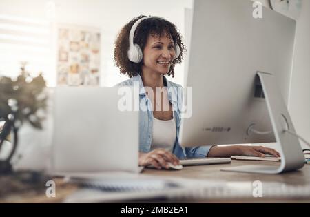 Ich arbeite an meinem Blog. Eine attraktive junge Frau, die allein zu Hause sitzt und ihren Computer benutzt, während sie Kopfhörer trägt. Stockfoto