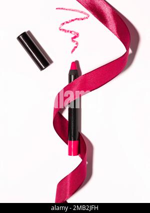 Roter matter Lippenstift in Form eines Bleistifts mit rotem Band, schmierter Textur auf weißem Hintergrund Stockfoto