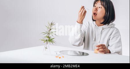 Eine Asiatin tropft cbd-Öl in den Mund. Pharmazeutische Pillen, Kapseln auf einem weißen Tisch. Konzept der Melatoninproduktion und Wiederherstellung von Schlaftabletten Stockfoto