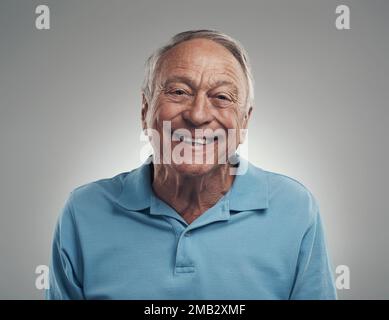 Du machst mich so glücklich. Ein Mann, der in einem Studio vor grauem Hintergrund glücklich in die Kamera lächelt. Stockfoto