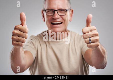 Daumen hoch für gute Stimmung. Ein gut aussehender, reifer Mann, der im Studio vor grauem Hintergrund steht und eine Daumen-hoch-Geste macht. Stockfoto