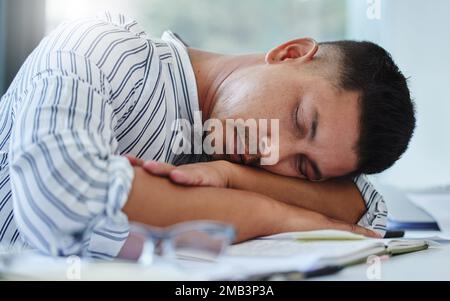 Ist es schon Wochenende? Ein junger Geschäftsmann, der erschöpft ist und auf seinem Schreibtisch in seinem Büro schläft. Stockfoto