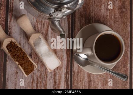 Zenithaler Blick auf eine Kaffeetasse mit Milchkännchen und Holzlöffeln auf einem Holztisch mit Textfläche Stockfoto