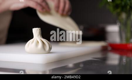 Die Hände des Küchenchefs Formen Khinkali vor dem Hintergrund handgefertigter Schneidebretter. Köstliche hausgemachte Speisen, georgianische Küche. Die Chefköchin bereitet sich vor Stockfoto