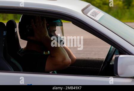 William Jarrell, der einen 1994 BMW 325 fährt, passt seinen Helm an, während er während eines Autocross-Events in der Marine Corps Air Station Cherry Point, North Carolina, am 11. Juni 2022 an die Startlinie fährt. Der Sports Car Club of America und das Single Marine Program veranstalten Autocross, damit Mitglieder des Dienstes und Automobilfans ihre Fahrzeuge in einer sicheren Umgebung bis an ihre Grenzen fahren können. Stockfoto