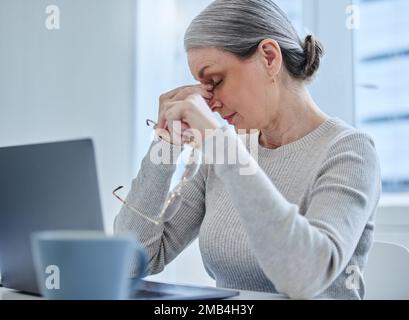 Kann ich das einfach hinter mich bringen? Eine reife Geschäftsfrau, die allein im Büro sitzt und Kopfschmerzen hat. Stockfoto