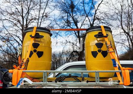 Zwei gelbe Metallfässer mit Schildern für Radioaktivität auf dem Dachgepäckträger, die mit Spanngurten befestigt sind, Transport nuklearer Abfälle, radioaktiver Abfall Stockfoto