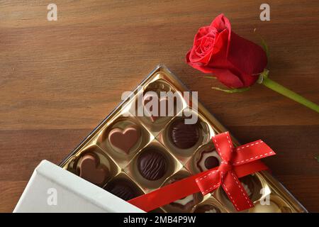 Romantisches Geschenk mit einer Schachtel Pralinen mit roter Schleife und Rose auf einem Holztisch. Draufsicht. Stockfoto