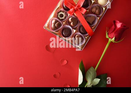 Festlicher Hintergrund mit einer Auswahl an Pralinen und roten Rosen mit Herzen auf rotem Hintergrund. Draufsicht. Stockfoto