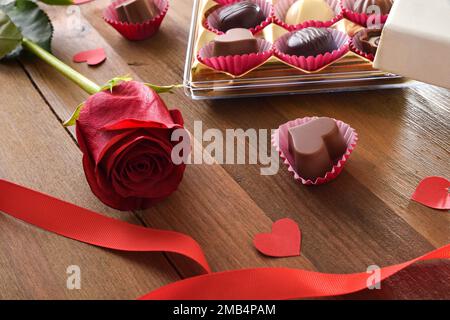 Romantischer Hintergrund mit einer Schachtel Pralinen auf einem rustikalen Holztisch mit einer roten Rose. Erhöhte Aussicht. Stockfoto
