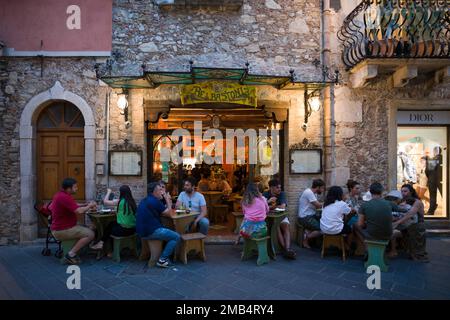 Gäste sitzen vor dem Restaurant, Cafe Bastoni, Abendstimmung, auf der rechten Seite des Ladens Christian Dior, Corso Umberto, Altstadt von Taormina, Sizilien Stockfoto