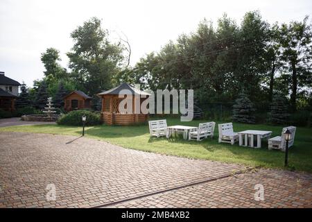 Innendesign der Sommerpavillon am See mit stilvollem Rattan-Sessel, Couchtisch, Sofa, Kissen, Karo und eleganten Accessoires in moderner Einrichtung. Sommerliche Stimmung. Hochwertiges Foto Stockfoto