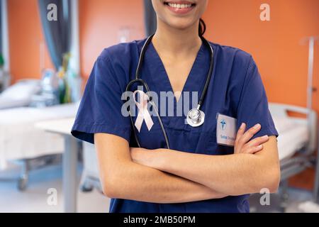 Die Mitte einer lächelnden birassischen Ärztin, die ein Krebsband auf der Krankenhausstation trägt Stockfoto