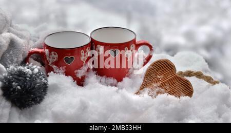 Zwei rote Tassen mit hölzernem Herz im Schnee - valentinskonzept Stockfoto