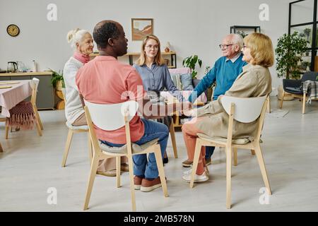 Ältere Menschen, die Unterstützung in der Psychotherapie-Sitzung bekommen, sitzen im Kreis und halten Händchen Stockfoto