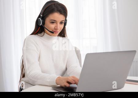 Eine junge, schöne Frau mit Kopfhörern engagiert sich im Online-Unterricht. Unterricht im Online-Konzept Stockfoto